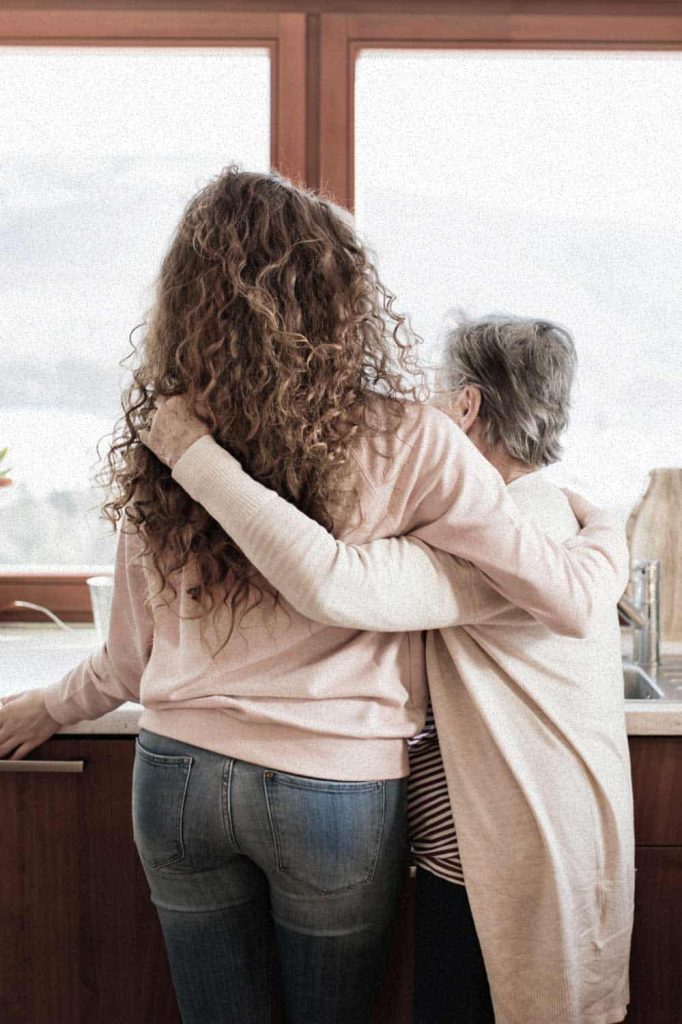Two women embracing at a kitchen window