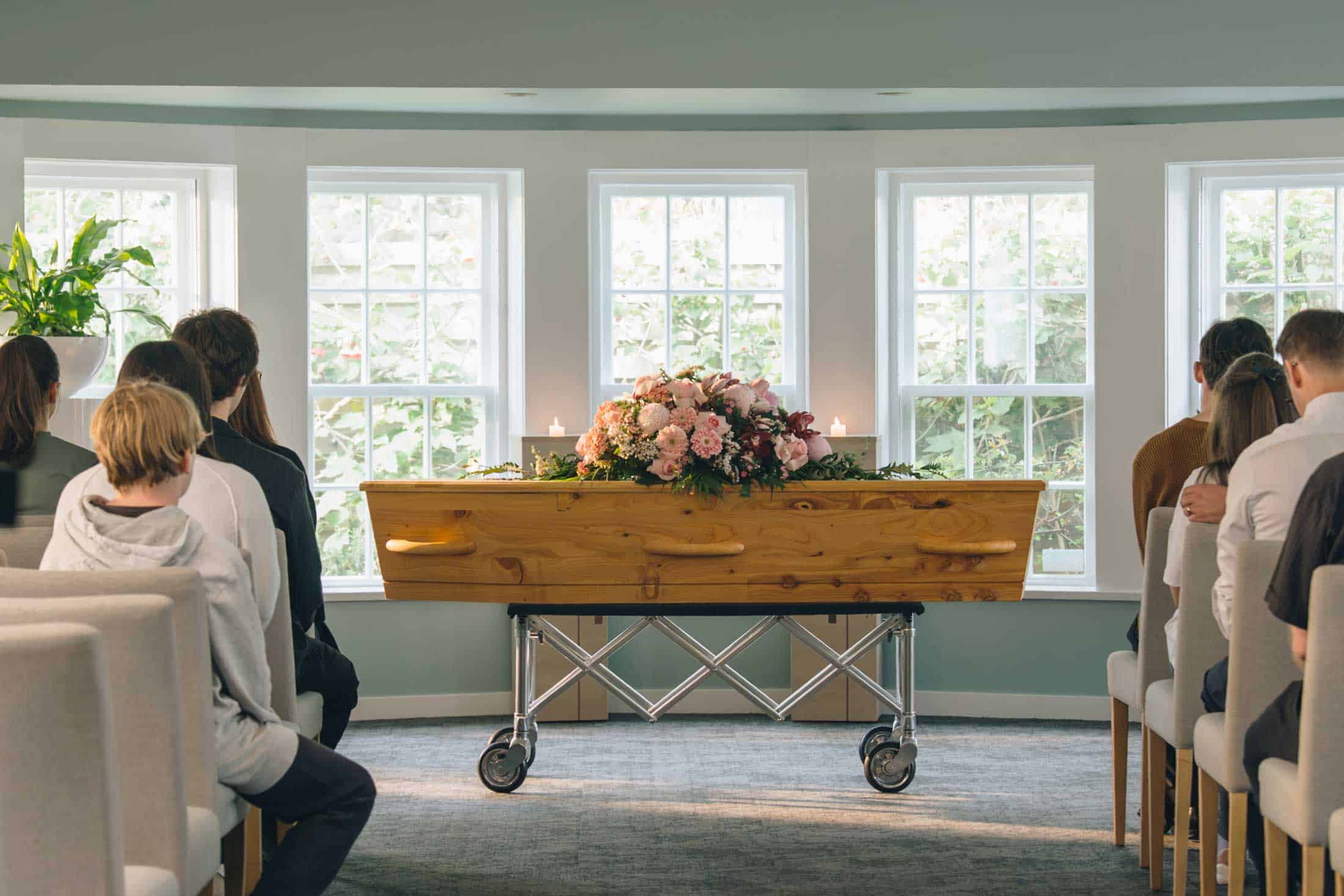 Family and friends seated in a Lychgate chapel, facing a casket with flowers