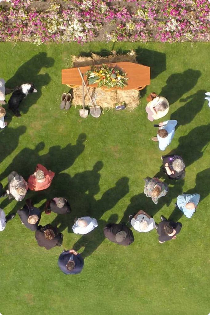 Family and friends gathered in a circle around a casket on a lawn, seen from above